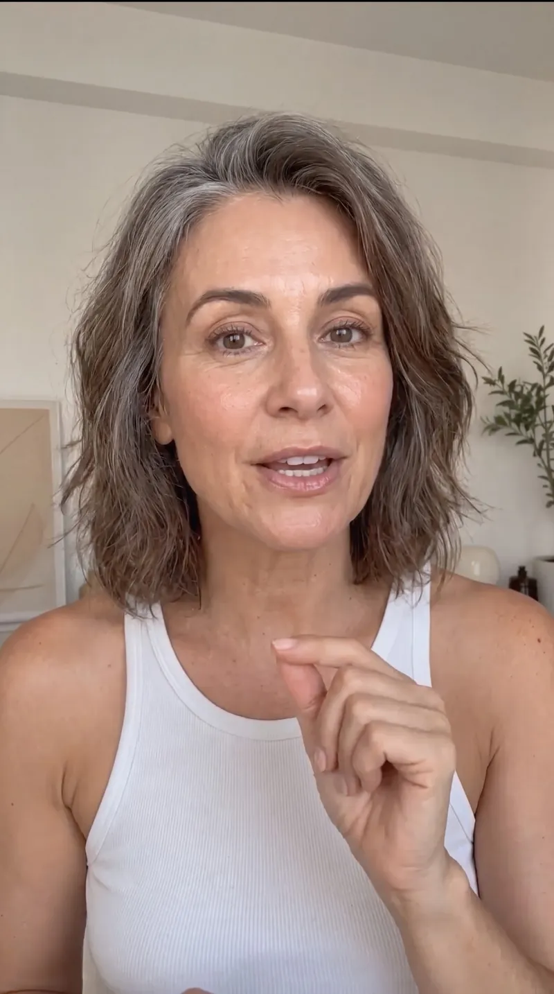 Image faite avec Nano Banana Pro : selfie façon UGC d’une femme d’une cinquantaine d’années aux cheveux gris qui parle face caméra chez elle